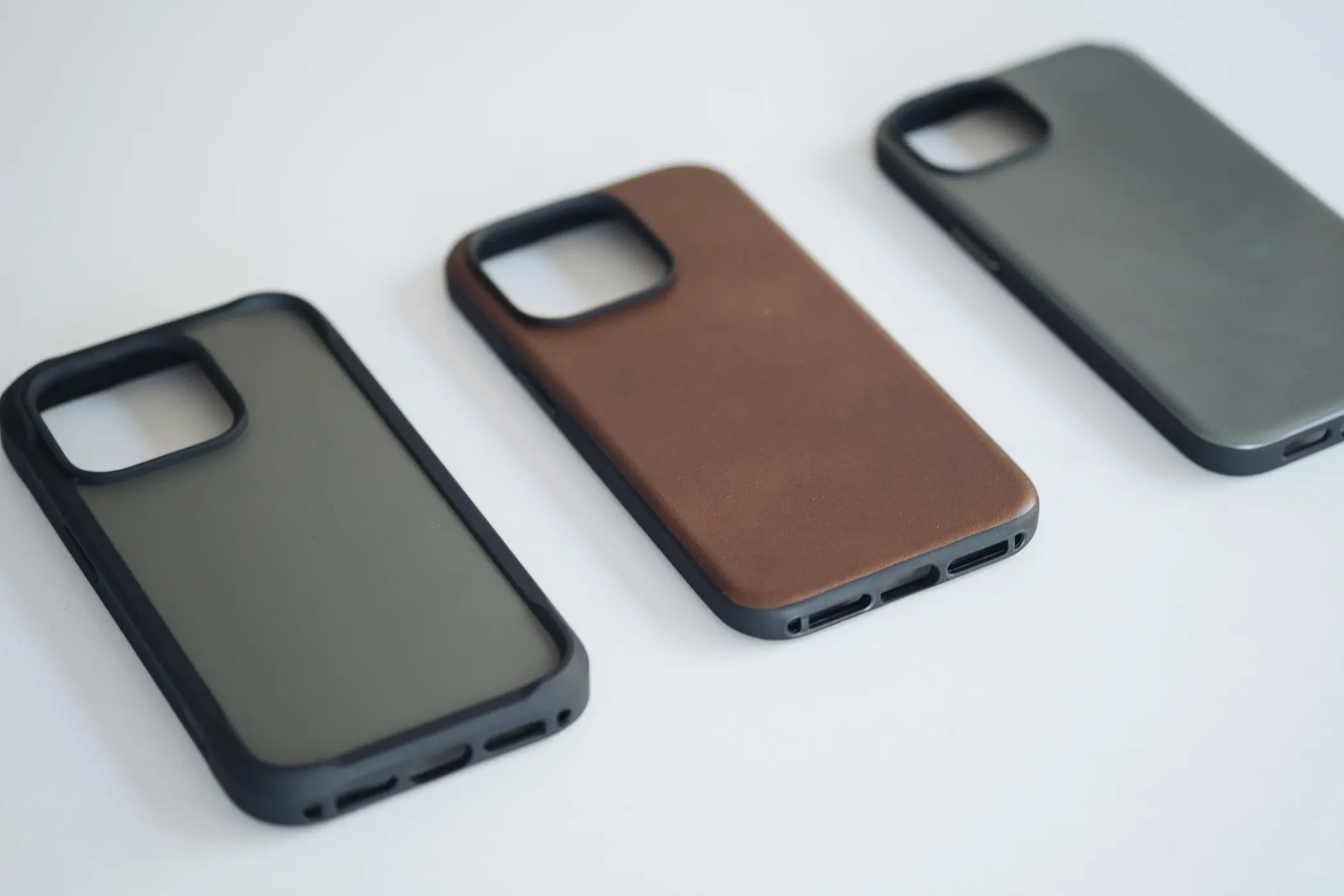 Green, leather and grey iphone 14 cases laying on a white table