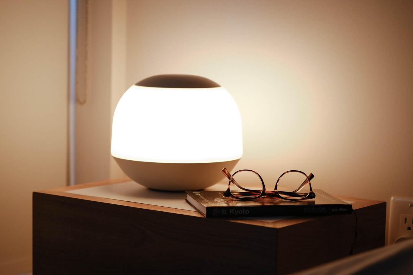 Soft light on a bedside table with a book and eye glasses visible